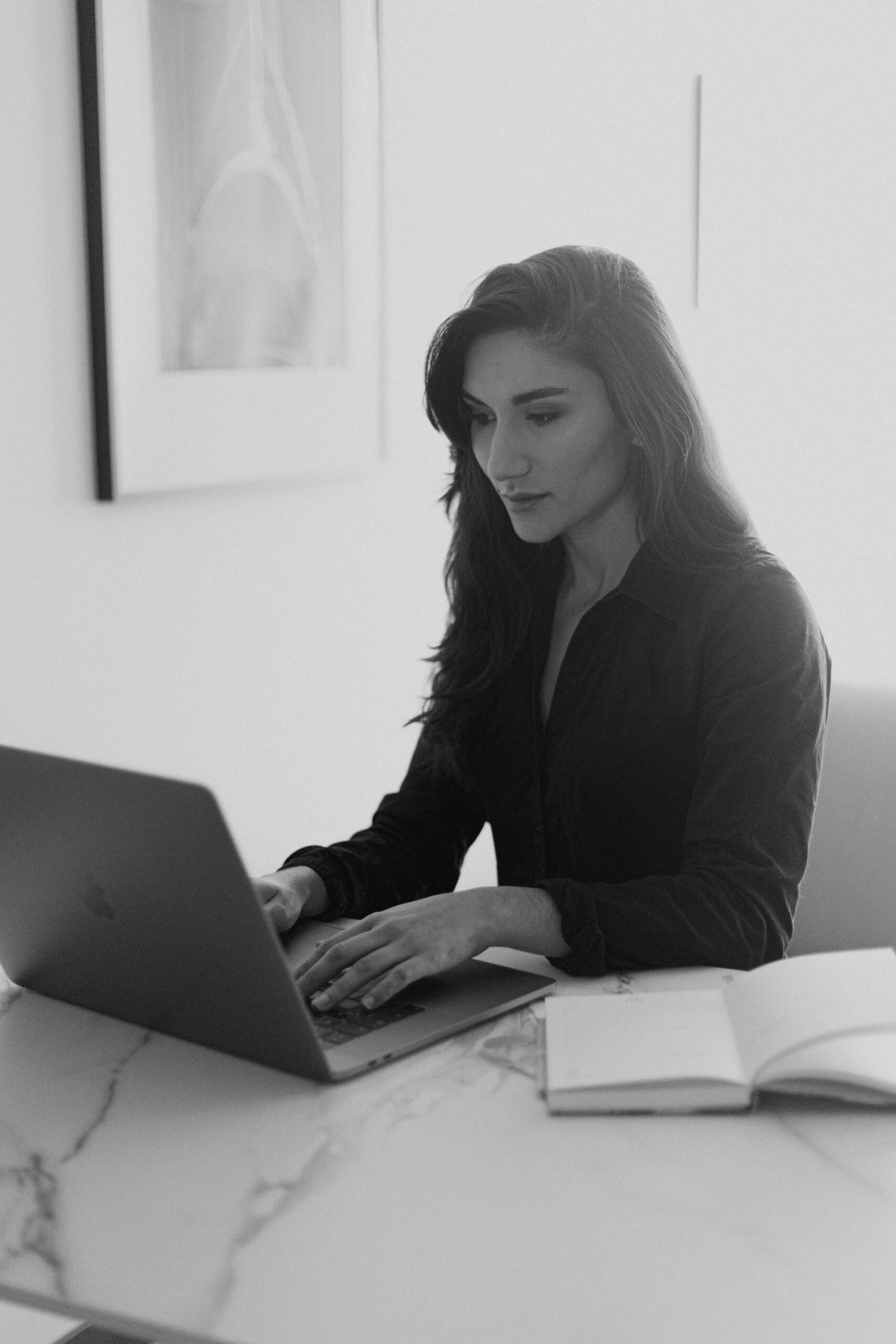 Black and white photo of a woman working on a laptop in an office setting.