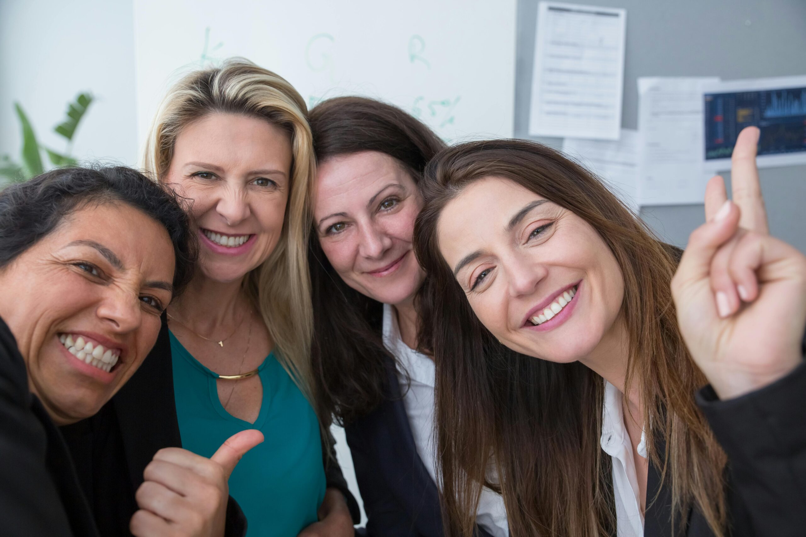 Four female colleagues smiling and posing for a group photo at the office, exuding teamwork and positivity.